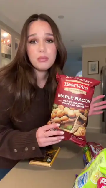 A woman in her kitchen holding up a bag of maple bacon chips