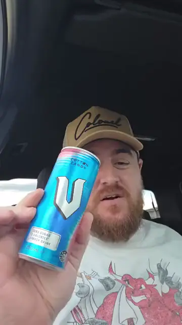 A man in a cap sitting in his car holding up a can of energy drink